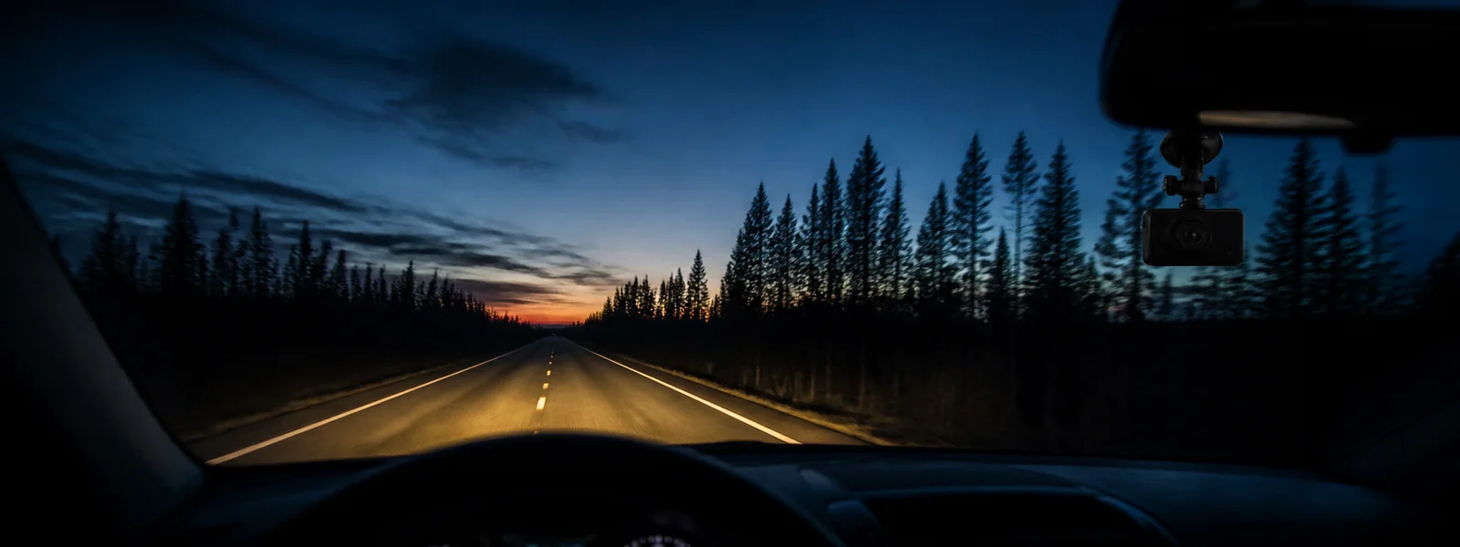 Autokamera tuulilasissa hämärällä metsätiellä